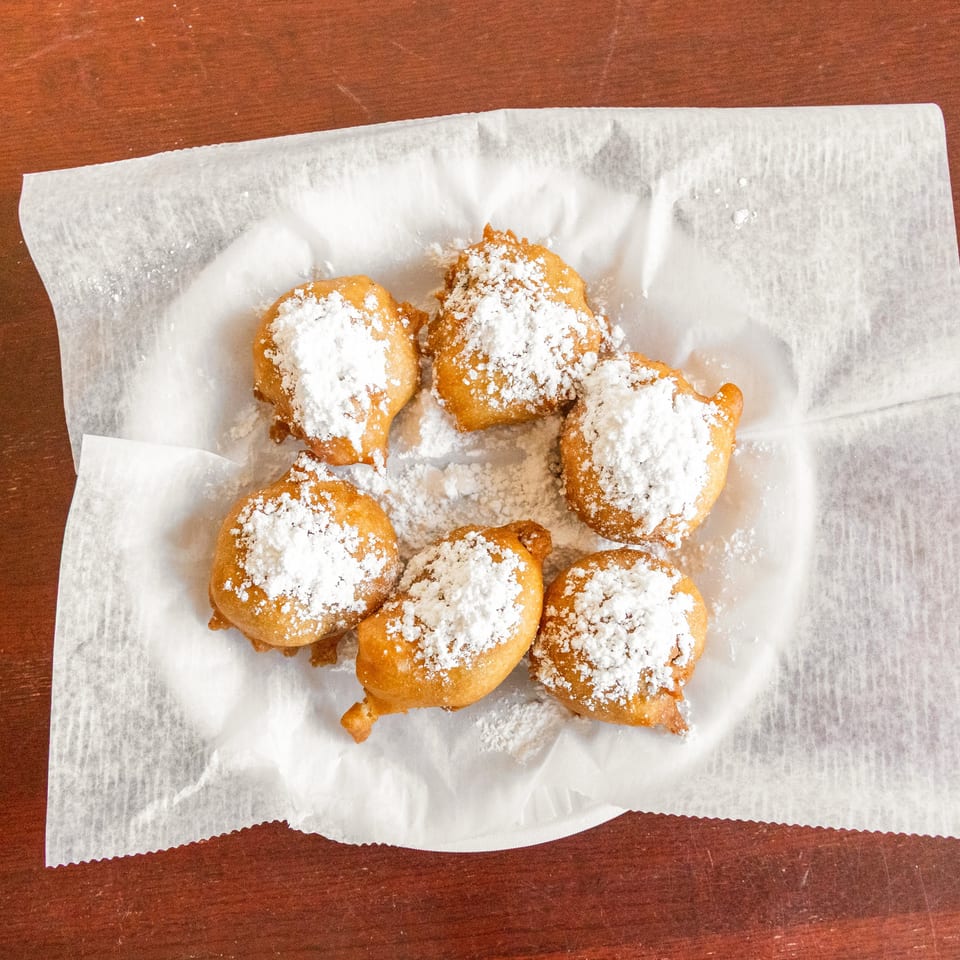 Golden fried dough bites generously dusted with powdered sugar, served on parchment paper over a wooden table.