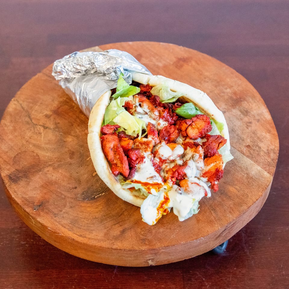 Loaded pita wrap with seasoned grilled meat, lettuce, and creamy sauce on a wooden serving board.