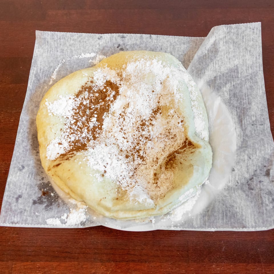 Stack of golden pancakes dusted with powdered sugar and cinnamon on wax paper atop a wooden table.