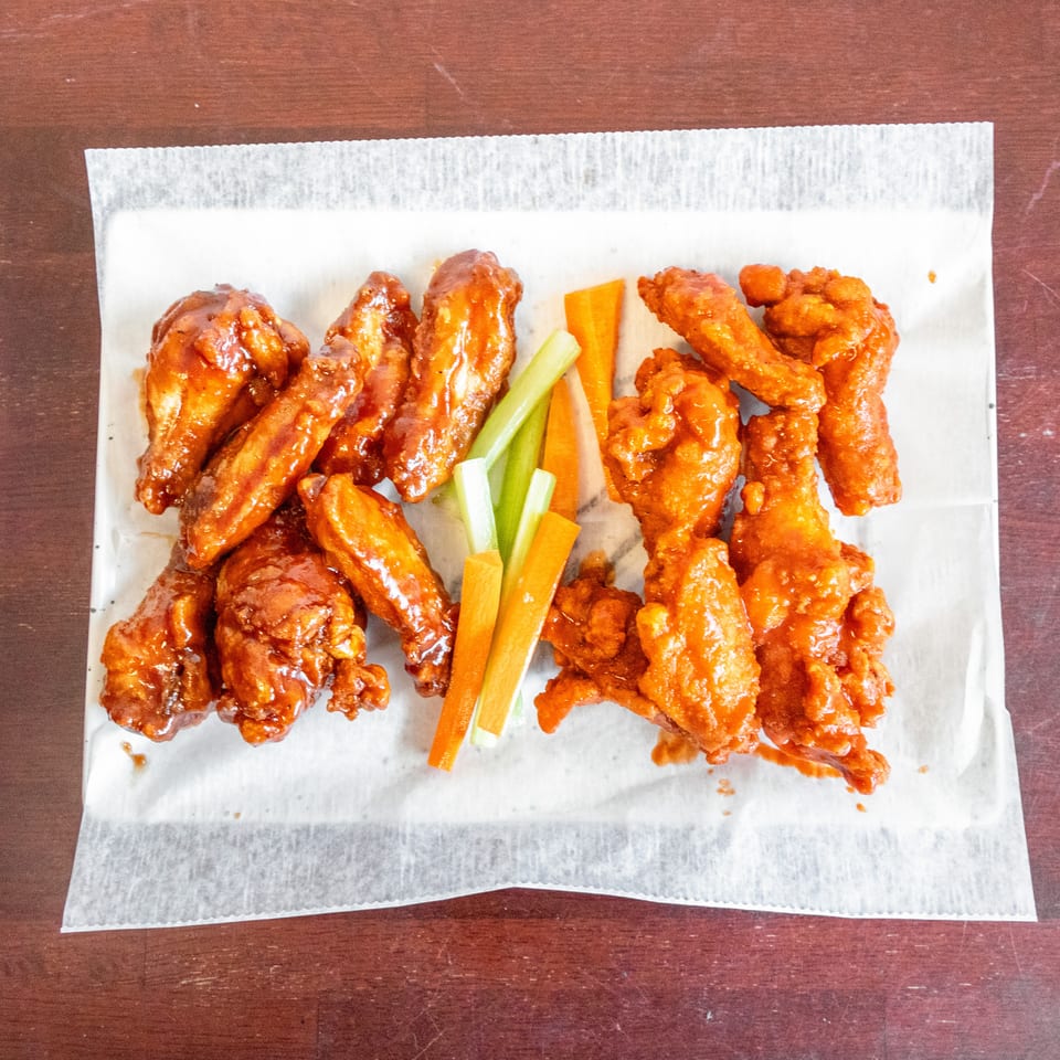 Saucy chicken wings and crispy chicken tenders served with carrot and celery sticks on a paper-lined plate.