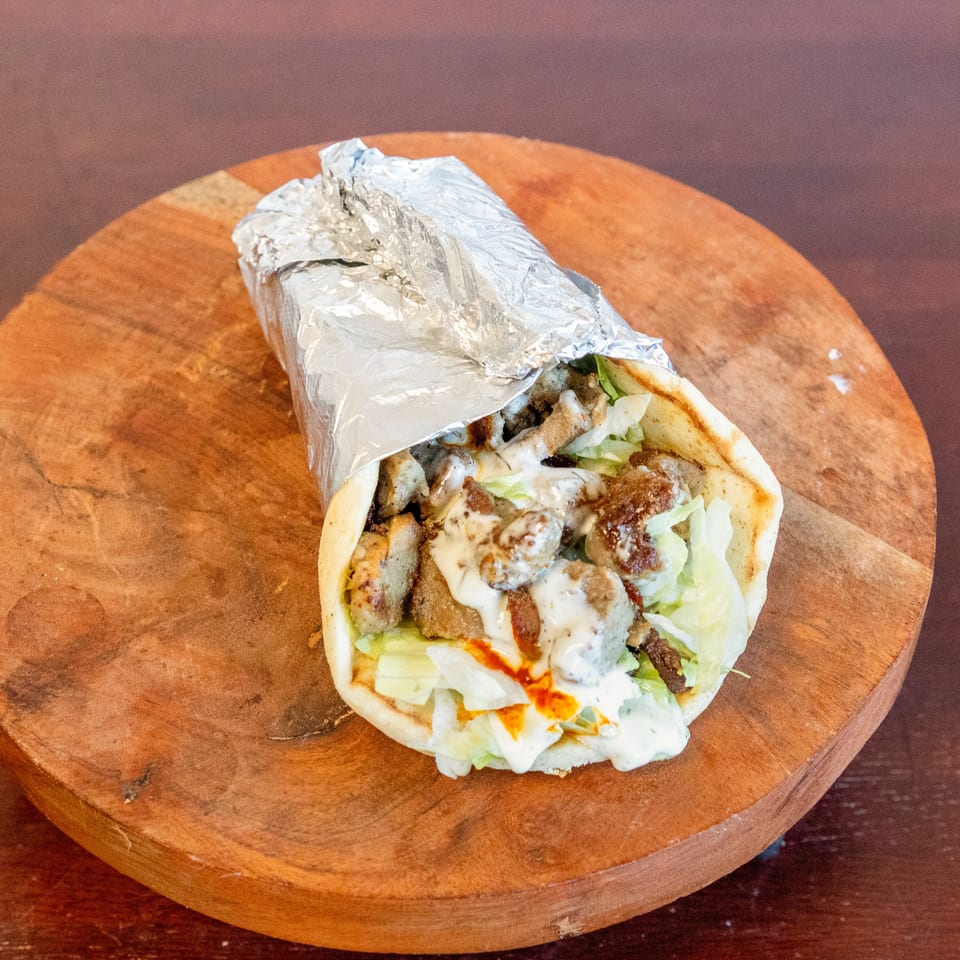 Foil-wrapped gyro pita filled with sliced meat, lettuce, and creamy sauce on a round wooden serving board.